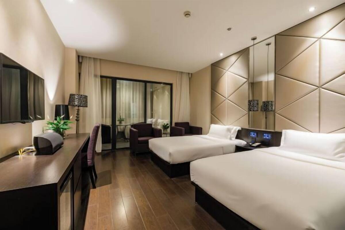 A hotel room with two beds, a desk, a chair, a TV, and a large mirror.