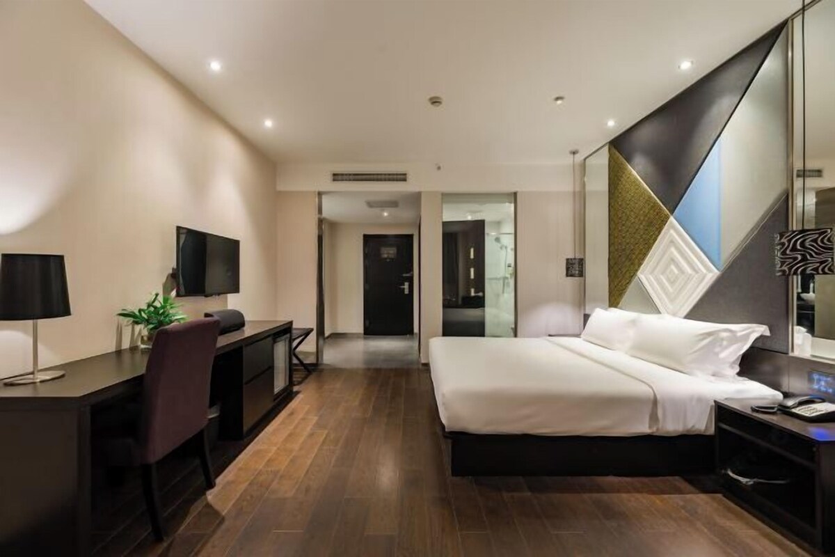 Une chambre d’hôtel moderne, dotée d’un grand lit, d’un bureau avec une chaise, d’une télévision et d’un grand miroir.