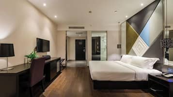 A modern hotel room with a large bed, a desk with a chair, a TV, and a large mirror.