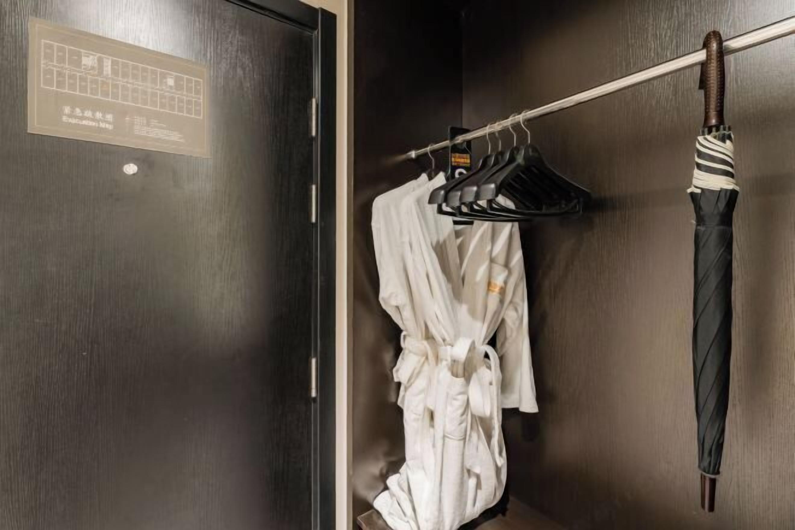 A wooden door with a sign, a white robe hanging on a rack, and a striped umbrella on a hook.