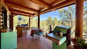 Un espacio comedor al aire libre con techo, una parrilla, mesas y sillas de madera, y vistas del paisaje circundante.