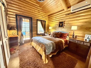 Cozy bedroom with a large bed, wooden walls, and a window with curtains.