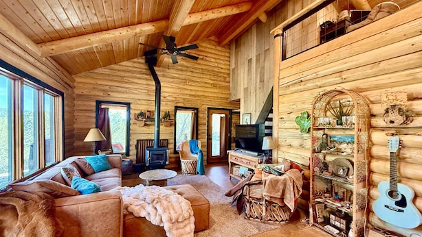 Acogedor interior de cabaña de madera con sofá, televisión, guitarra y chimenea.
