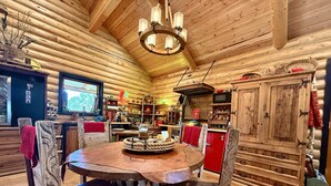 Un interior rústico de madera con una mesa redonda, sillas y un aparador rojo.