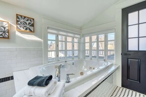 A modern bathroom with a large freestanding bathtub, a white tiled floor, and a door with a window. - 2BR/2BA • Sunny Retreat • Parks + Coffee Nearby (Portland)