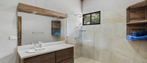 A bathroom with a wooden ceiling, a large mirror, a sink with a vanity, a shower area, and a small window.