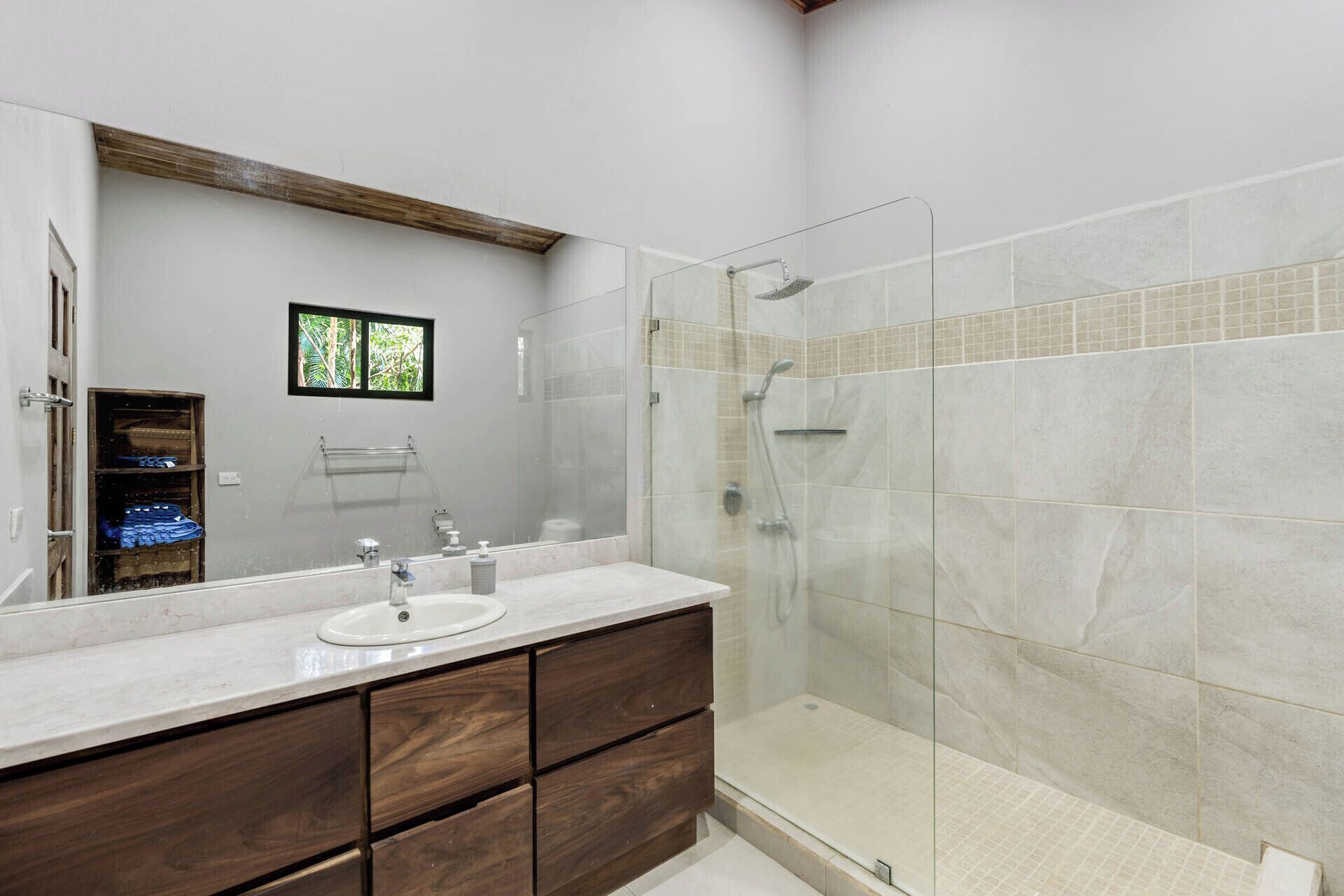 A bathroom with a large mirror, a sink, a shower, and wooden cabinets.