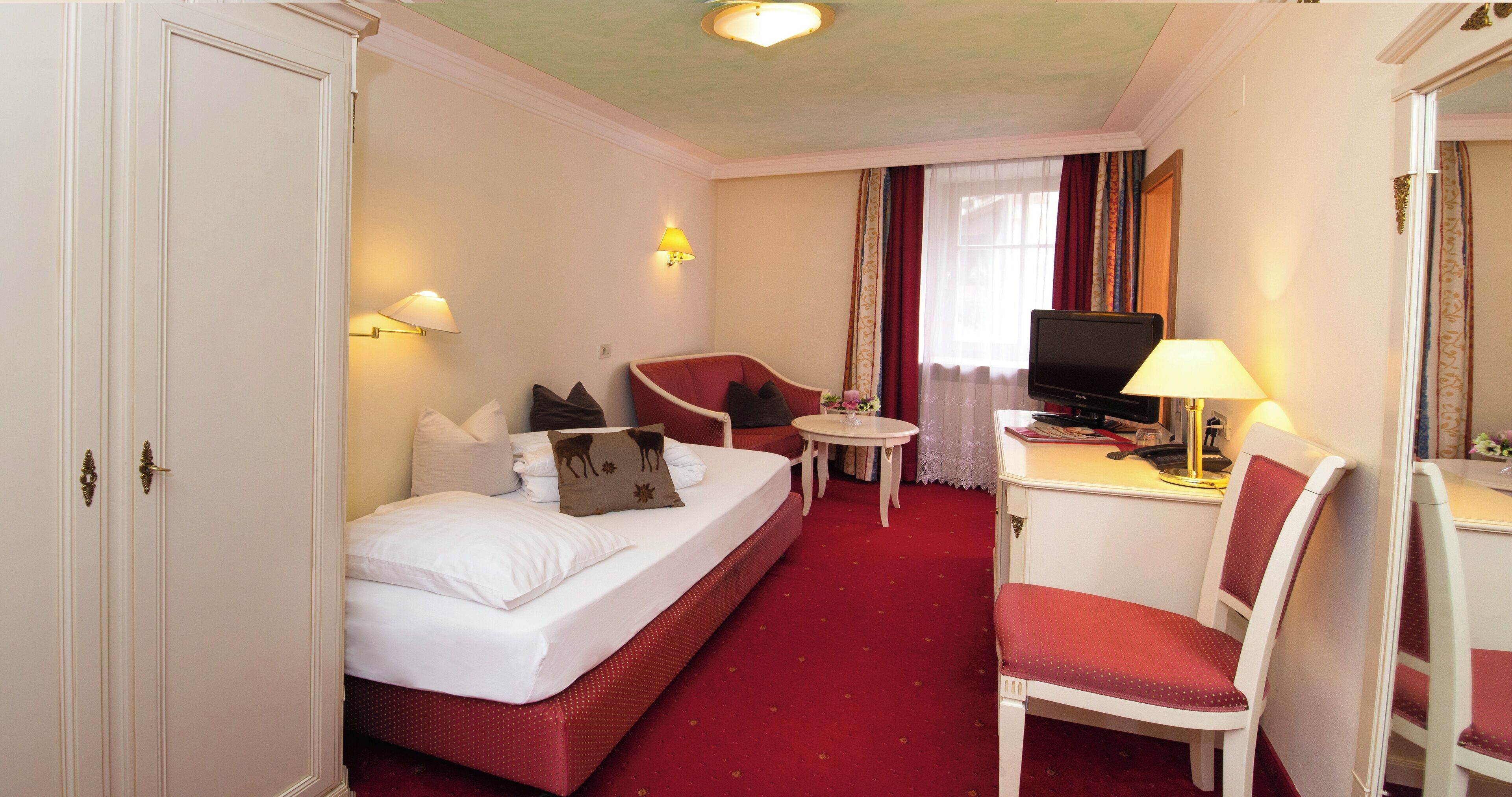 Ein Hotelzimmer mit einem Bett, einem Schreibtisch mit Stuhl, einem Fernseher und einem kleinen Tisch.