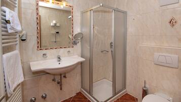 Un baño con ducha compartimentada por vidrio, un lavamanos con espejo y un inodoro.
