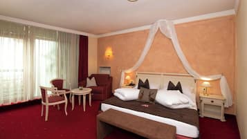 A hotel room with a large bed, a bench, two chairs, a small table, and a nightstand with a lamp.