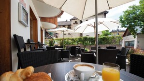A café with outdoor seating, a table with a cup of coffee, a glass of orange juice, and croissants. - Erlebnishotel Engel (Sluderno)