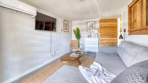 Un salon moderne avec un canapé, une table basse et un téléviseur. On y trouve également une plante et un panneau mural en bois.