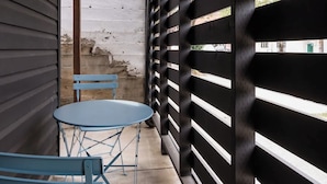 Un espace extérieur abrité, doté d’une table et de chaises, d’un plafond en bois et d’un mur noir orné de lattes horizontales.