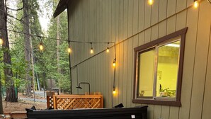 Een hottub met treden, omgeven door een houten terras, verlicht met lichtslingers, met een raam en uitzicht op bomen.