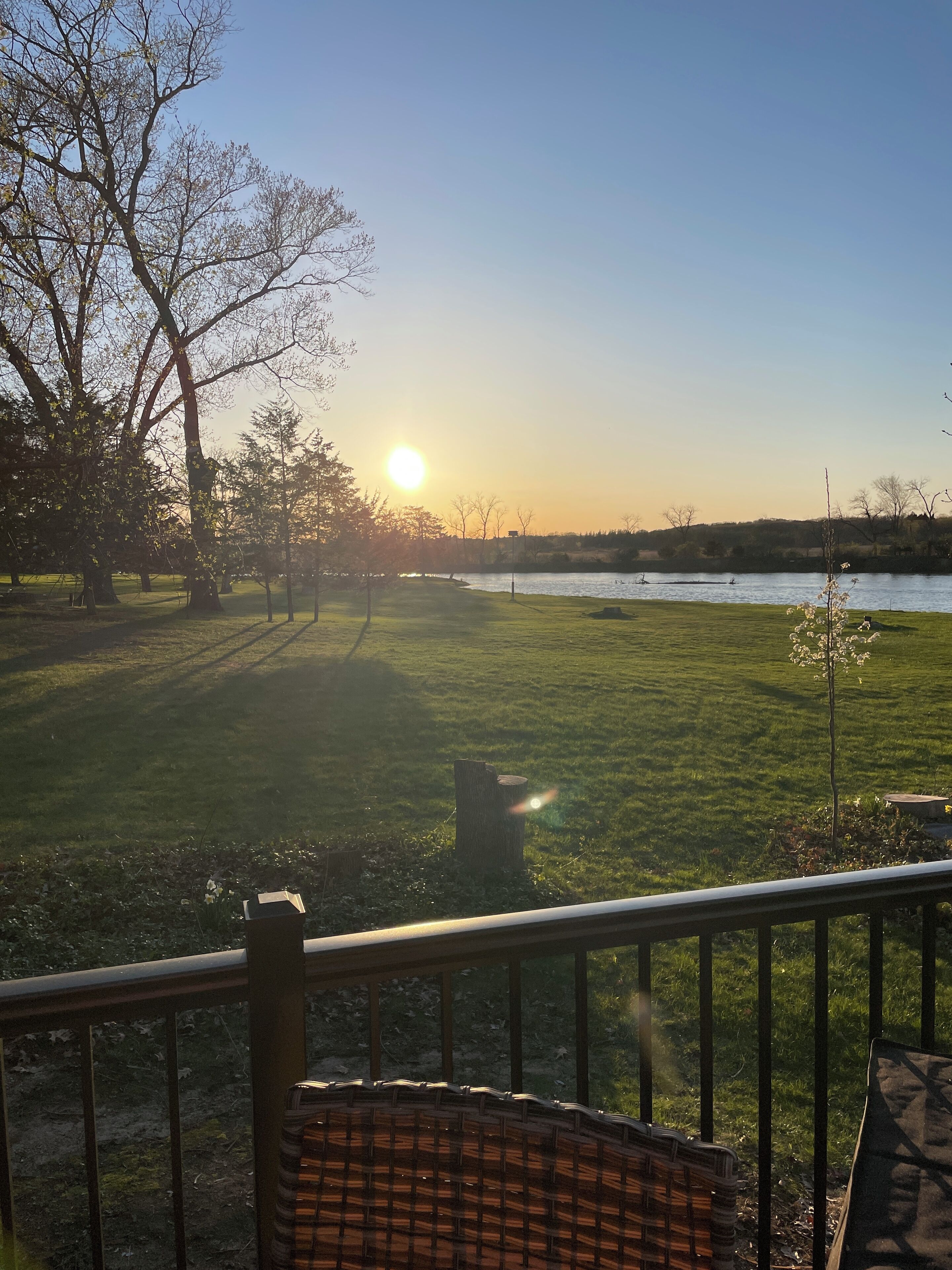 A view from a balcony overlooking a grassy area with a body of water, trees, and a clear sky.