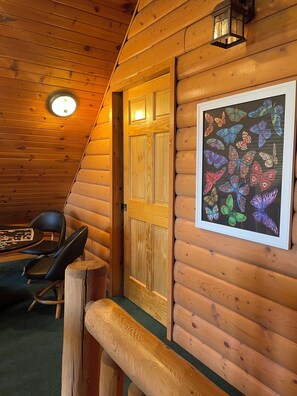 L’intérieur chaleureux d’un chalet en rondins, avec une porte en bois, une œuvre d’art représentant un papillon encadré, une table ronde entourée de chaises et une lanterne suspendue au plafond.