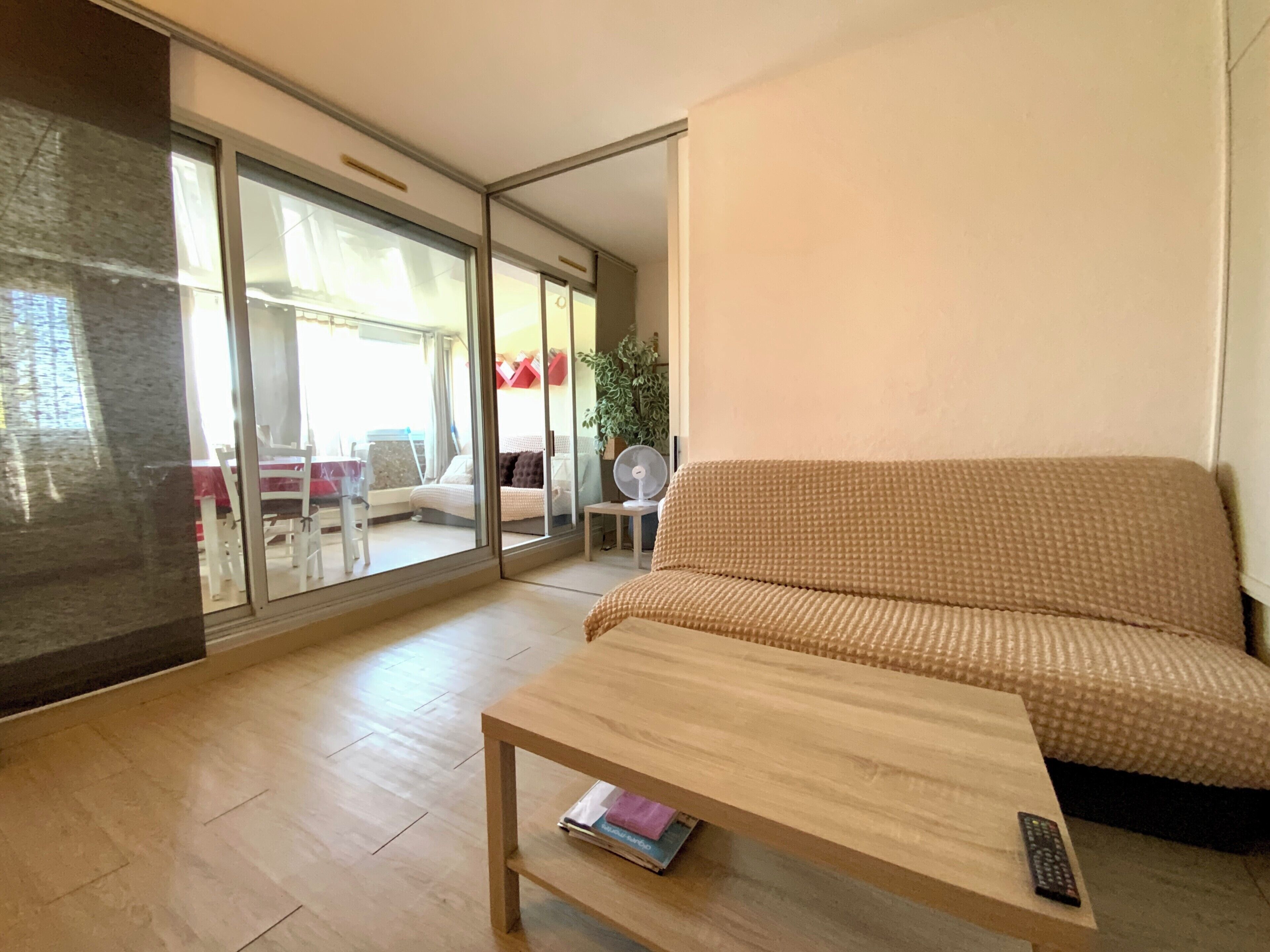 A modern living room with a wooden coffee table, a patterned sofa, and a sliding glass door leading to an outdoor dining area.