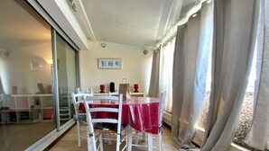 A dining area with a table covered in a red tablecloth, white chairs, and a glass partition.