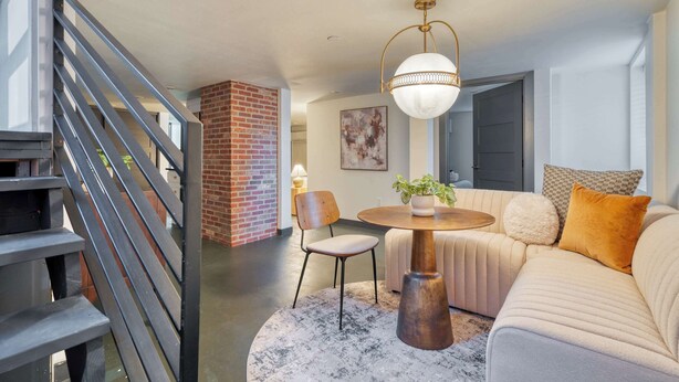 A modern living room with a staircase, a round wooden table, a beige sofa, and a potted plant. - Renovated 2BR Garden Suite • Steps to NW 23rd (Portland)
