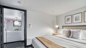 A modern hotel room with a large bed, a bedside table with a lamp, a headboard with a woven design, and framed artwork on the wall. - Renovated 2BR Garden Suite • Steps to NW 23rd (Portland)