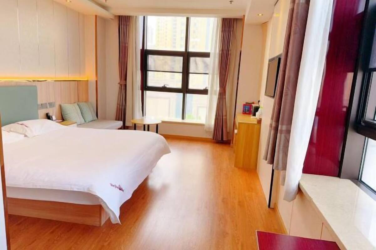 Habitación de hotel con una cama grande, una mesita pequeña, una ventana con cortinas y vistas a la ciudad.