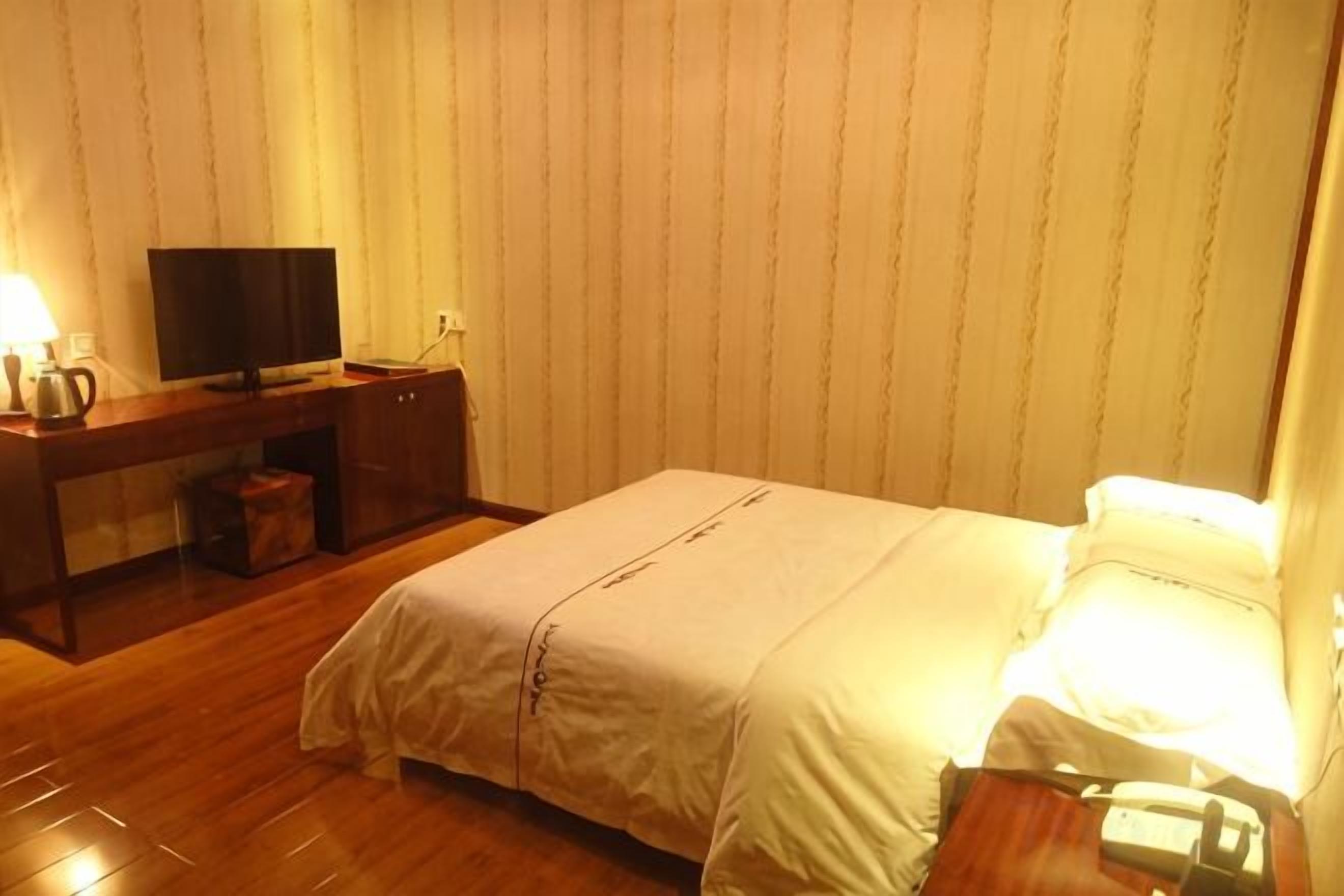 A hotel room with a bed, a desk, a television, and a lamp.