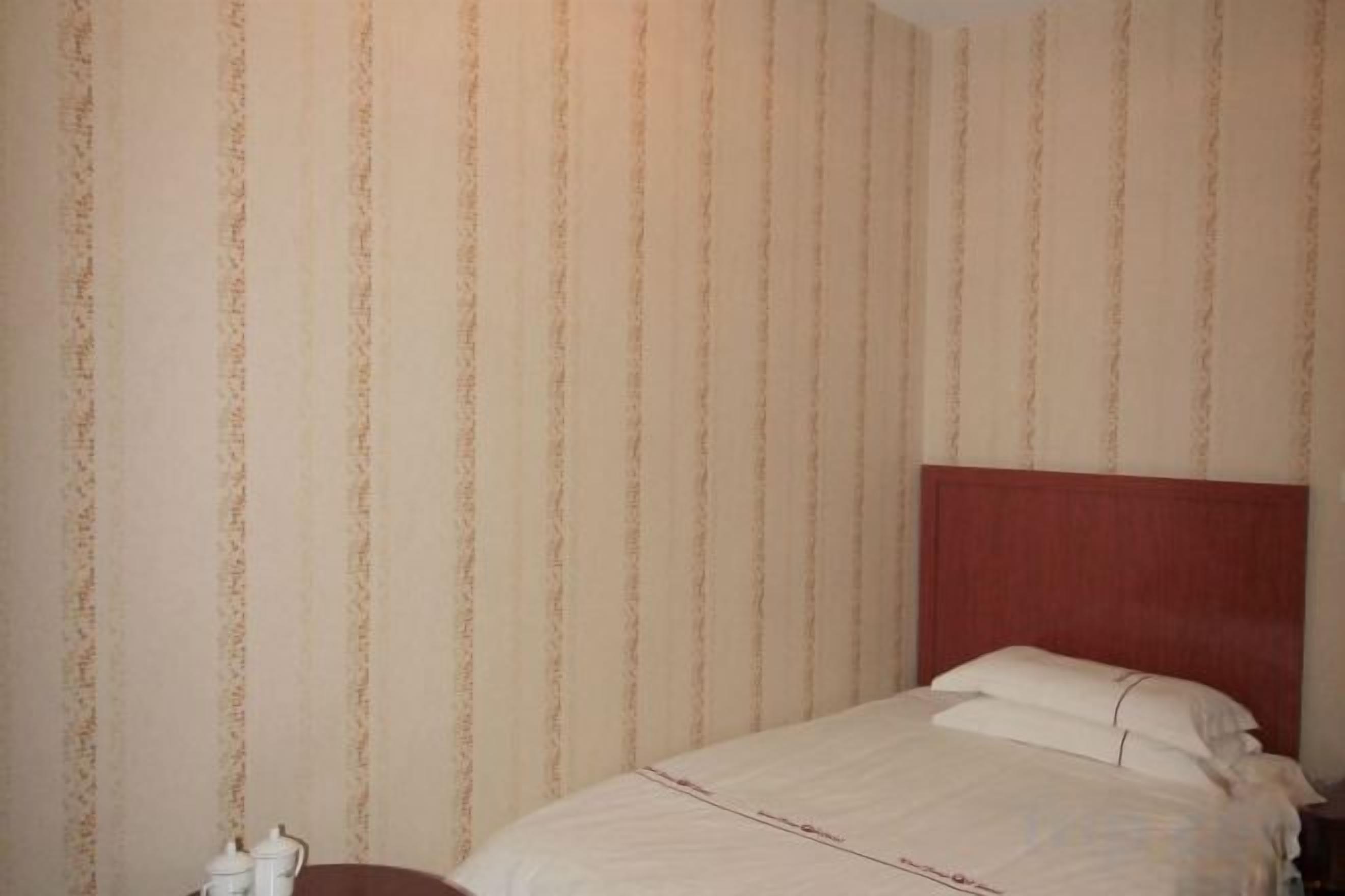 A single bed with a wooden headboard in a room with striped wallpaper.