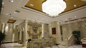 Un vestíbulo de hotel con una recepción, un candelabro imponente, suelo de mármol y una escalera.