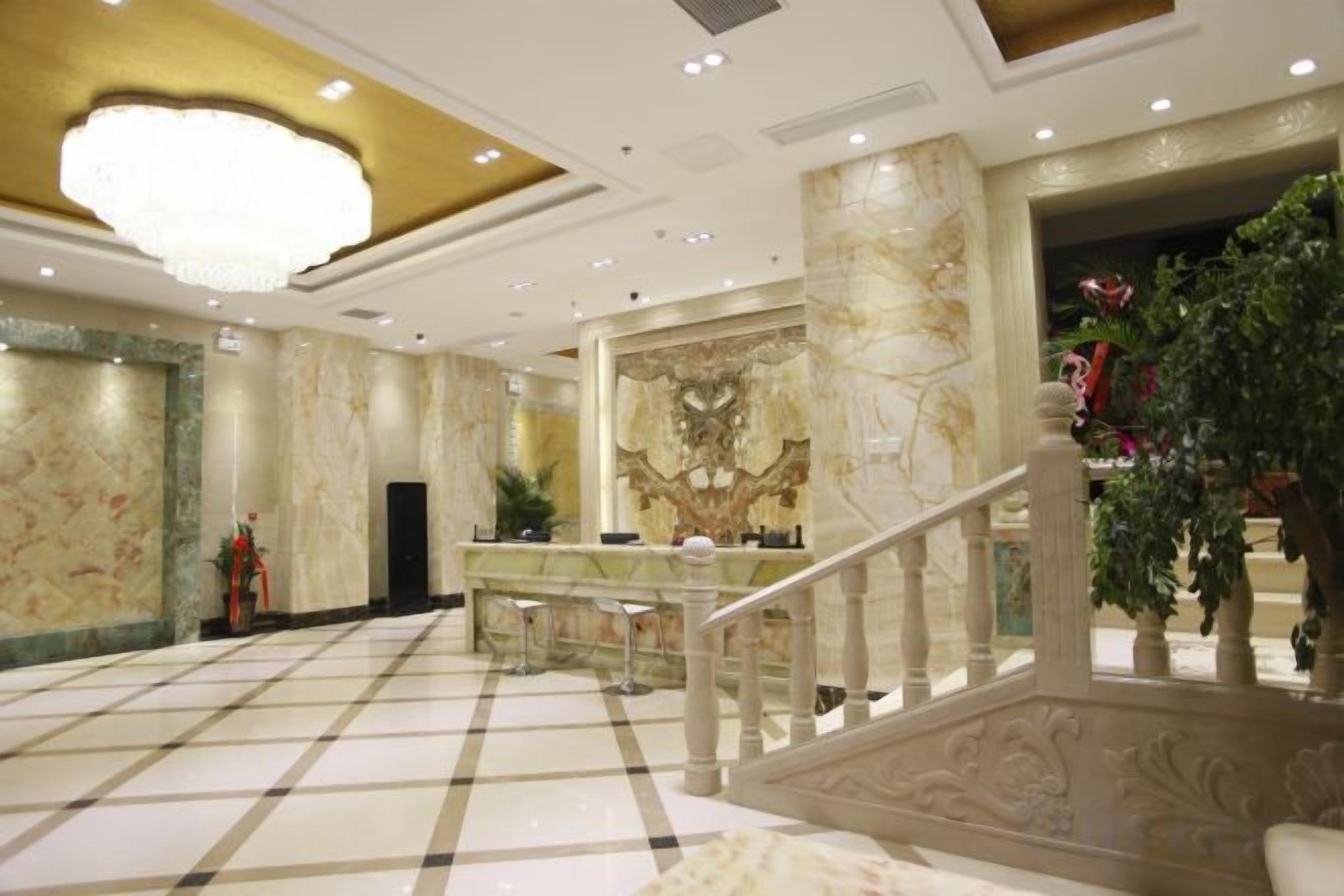Un hall de hotel con piso de mármol, un mostrador de recepción, una escalera y un candelabro.