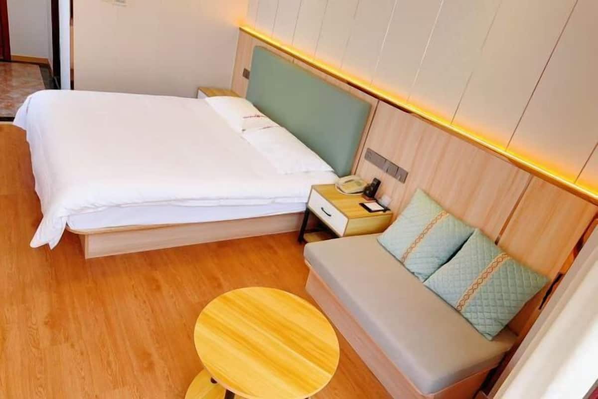 Habitación de hotel con cama, mesita de noche, lámpara y una pequeña mesa de madera.