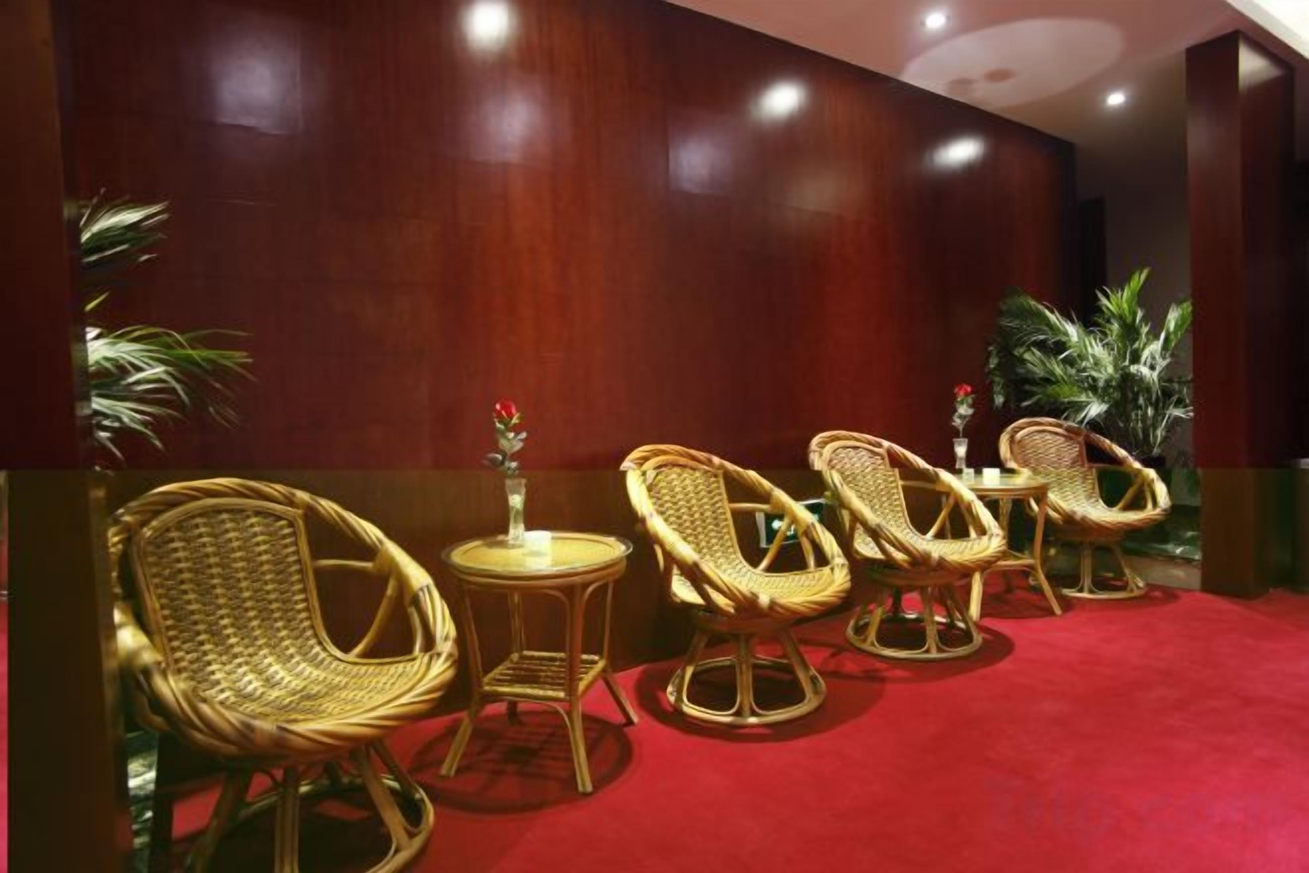 A room with wicker chairs and a small table, a red carpet, and a wooden wall.
