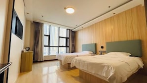 Habitación de hotel con dos camas, un panel de pared de madera, una ventana con cortinas, una mesita de noche y un televisor de pantalla plana montado en la pared.