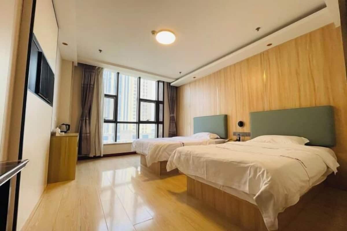 Habitación de hotel con dos camas, un panel de pared de madera, una ventana con cortinas, una mesita de noche y un televisor de pantalla plana montado en la pared.