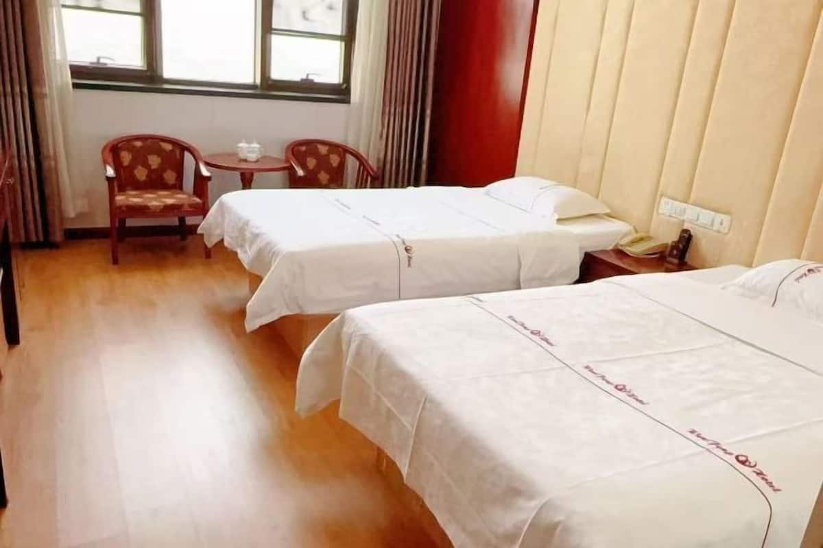 Habitación de hotel con dos camas, una mesita, dos sillas, un ventanal y una pared roja.