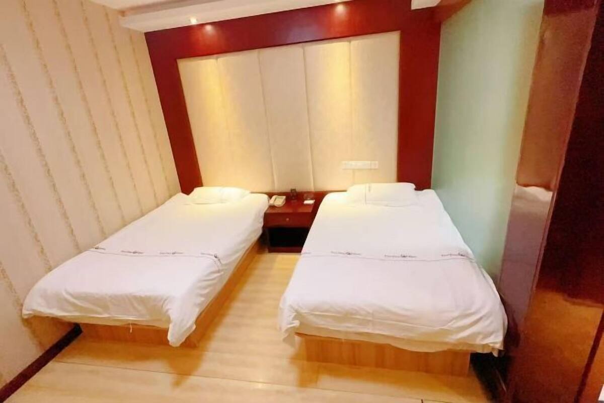 Una habitación con dos camas individuales, piso de madera, una mesita de noche con lámpara y una pared de acento roja.