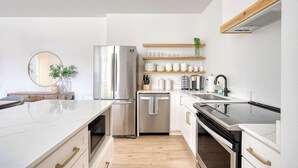 Een moderne keuken met een roestvrijstalen koelkast, vaatwasser en een zwarte oven. Er zijn witte kasten, een houten aanrecht en een houten plank boven de gootsteen.