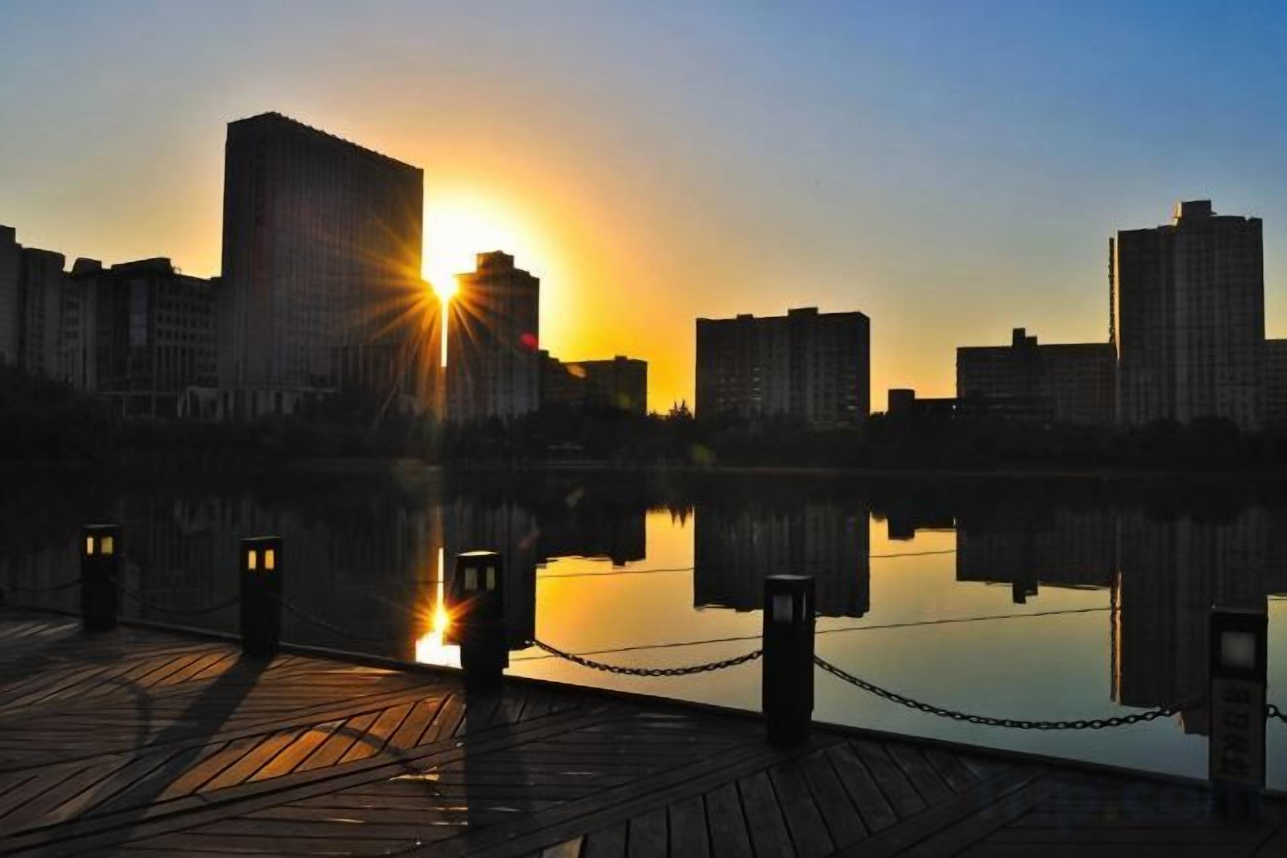 A waterfront view with a wooden dock, chain-link railing, and buildings in the background.