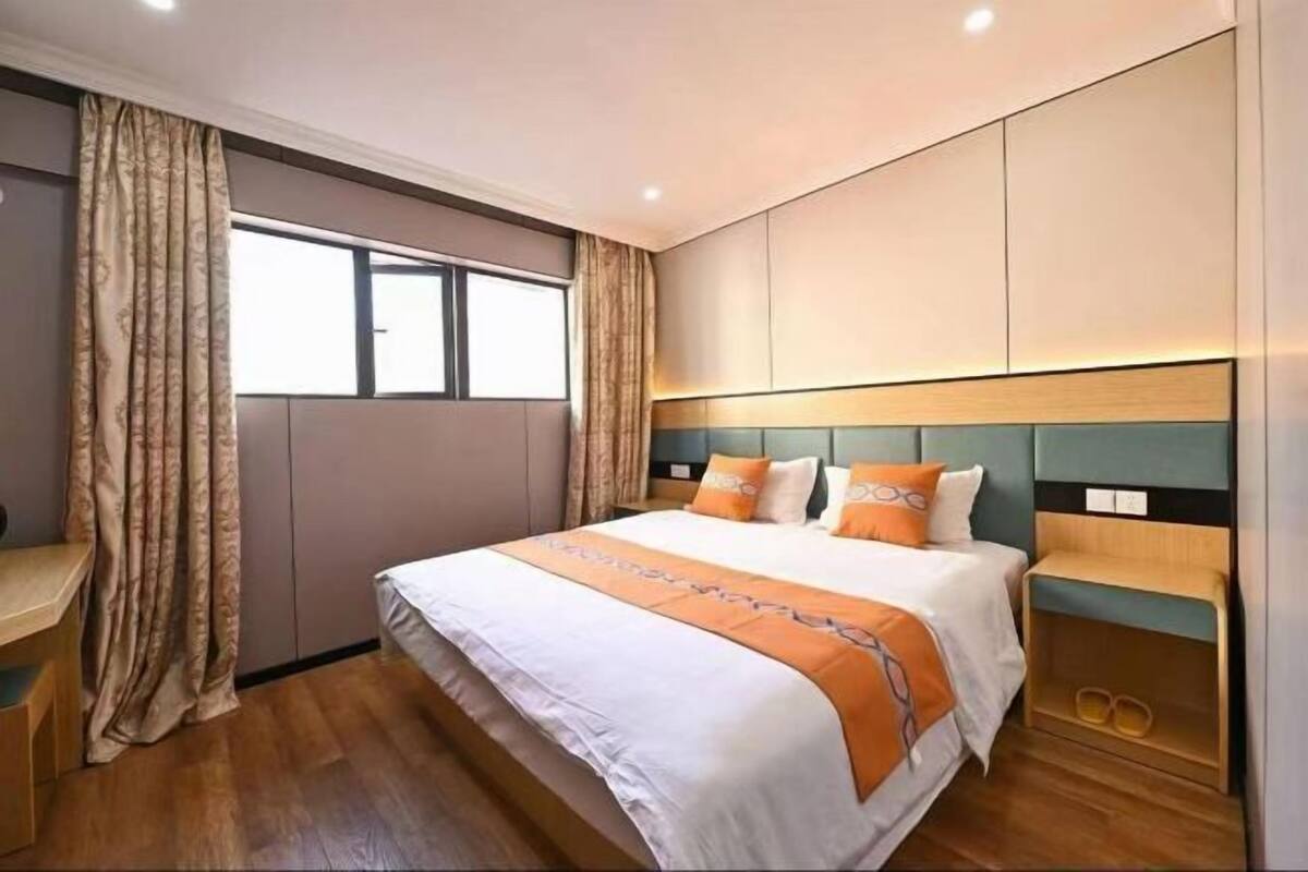A hotel room with a bed, curtains, a desk, and a view of the outside.