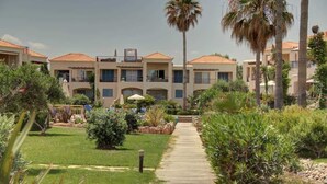 A hotel with multiple-story buildings, a central courtyard with a pathway, and palm trees. - Villa Elias 1BR Upper Apt with Pool (Maleme)