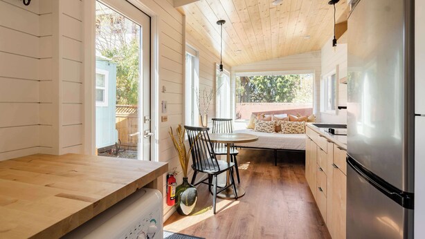 A kitchen with wooden cabinets, a stainless steel refrigerator, a dining table with chairs, and a view of the outside. - Classic 1920s Alberta Home + 2 Tiny Homes (Portland)