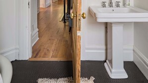 A bathroom with a white pedestal sink, a round mirror, and a wooden door frame. - Charming 2BR Walk-Up Steps to NW 23rd (Portland)