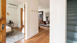 A modern interior with a wooden floor, a bed with a patterned rug, a dining area with chairs and a table, and a staircase. - Charming 2BR Walk-Up Steps to NW 23rd (Portland)