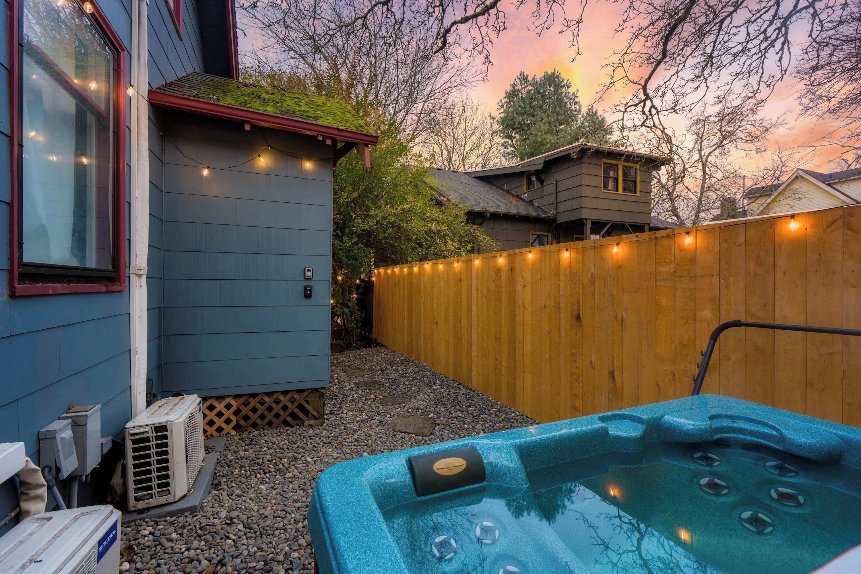 Een achtertuin met een hottub, een houten omheining en lichtjes.