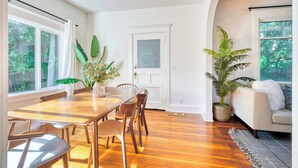 A dining area with a wooden table and chairs, a white door, and a large window with curtains. - 2BR/1BA • Big Yard • Near Moda Center | Hot Tub (Portland)