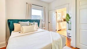A bedroom with a large bed, a teal headboard, and a view of the kitchen through an open door. - 2BR/1BA • Big Yard • Near Moda Center | Hot Tub (Portland)