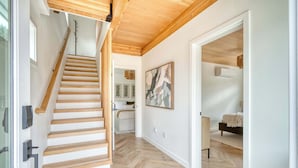 Un interior moderno con una escalera de madera, un pasillo que conduce a un dormitorio y un cuadro abstracto de gran tamaño en la pared.