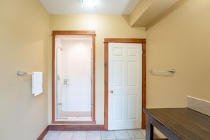 A hallway with a glass door leading to a shower area, a white door, and a wooden bench.