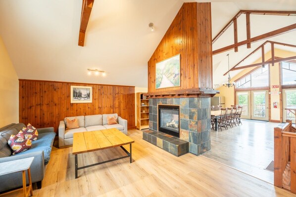 A spacious living room with a fireplace, wooden walls, and a dining area with natural light.