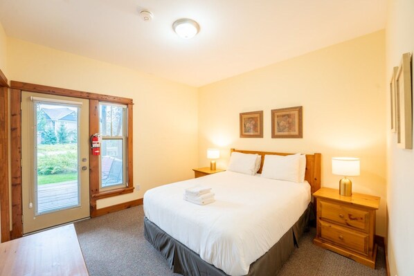 Une chambre d’hôtel avec un lit, deux tables de chevet, une porte donnant sur une vue agréable et un luminaire au plafond.