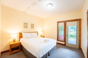 A hotel room with a bed, two bedside lamps, a door leading to a balcony, and two framed pictures on the wall.